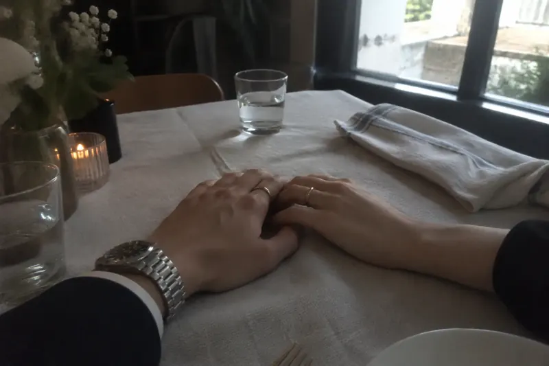 Two people holding hands across a sunlit restaurant table